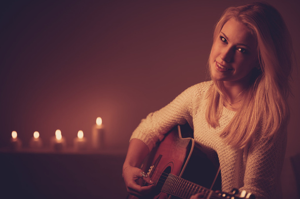Young blonde woman playing guitar in candle light - Foto, Bild