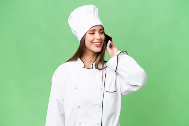 Young chef caucasian woman over isolated background keeping a conversation with the mobile phone - Φωτογραφία, εικόνα