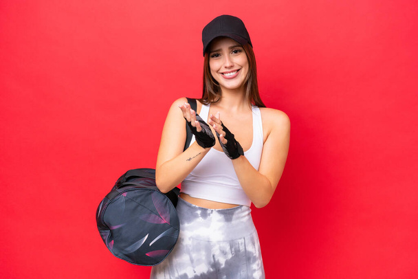 Young beautiful sport woman with sport bag isolated on red background applauding after presentation in a conference - Foto, afbeelding