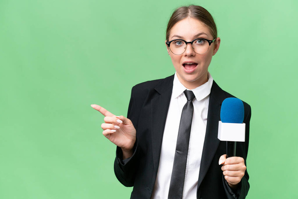 Young TV presenter caucasian woman  over isolated background surprised and pointing finger to the side - Fotoğraf, Görsel
