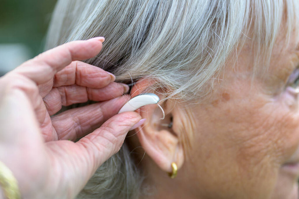 Older grey-haired deaf lady in her 80's with a hearing aid in her ear just putting it in - Fotó, kép