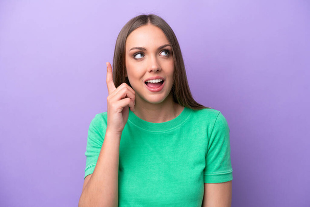 Young caucasian woman isolated on purple background intending to realizes the solution while lifting a finger up - Photo, Image