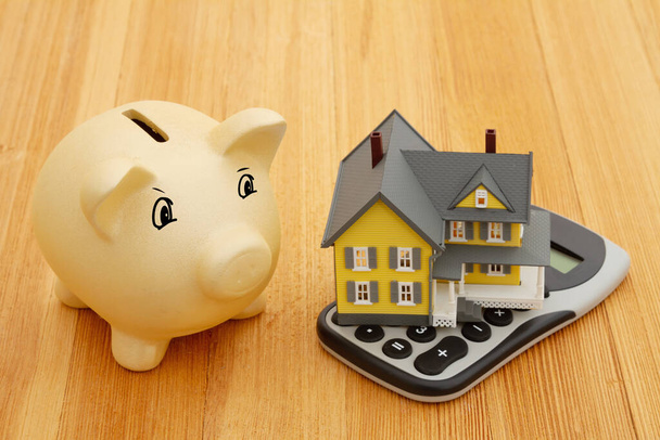 Mortgage calculator with a house on a calculator and piggy bank on a wood desk - Photo, image