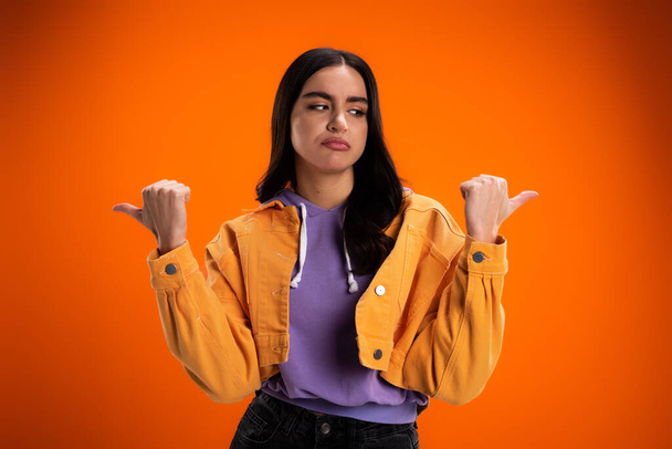 Skeptical brunette woman pointing with fingers isolated on orange - Foto, immagini