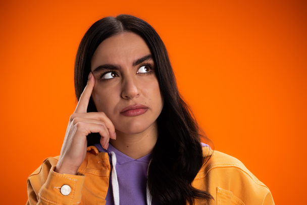 Portrait of pensive woman holding finger near eyebrow isolated on orange - Foto, afbeelding