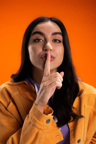 Portrait of brunette woman showing secret gesture isolated on orange - Foto, immagini