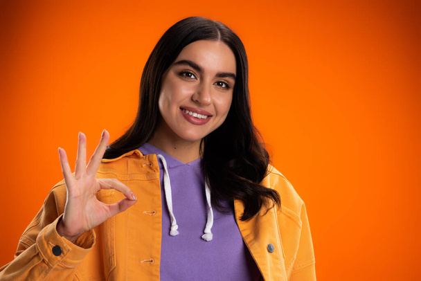 Portrait of smiling brunette woman showing ok sign isolated on orange - Foto, immagini