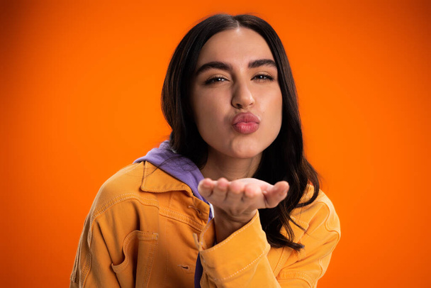Portrait of brunette woman blowing kiss at camera isolated on orange - Fotoğraf, Görsel