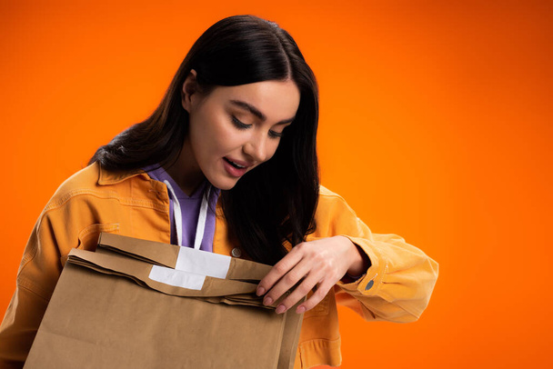 Pretty brunette woman holding takeaway paper bags isolated on orange - Fotó, kép