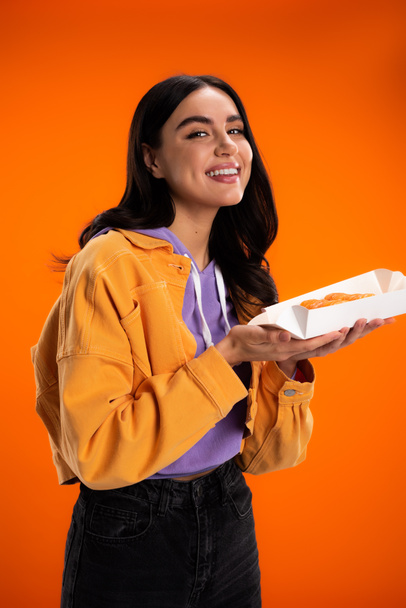 Positive woman holding takeaway sushi and smiling at camera isolated on orange - Photo, Image