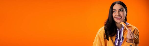 довольна брюнетка женщина, держащая сашими с палочками для еды и глядя в сторону изолированы на оранжевый, баннер - Фото, изображение