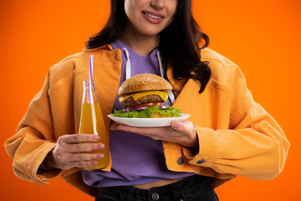 partial view of smiling woman with tasty burger and fresh lemonade isolated on orange - Photo, Image