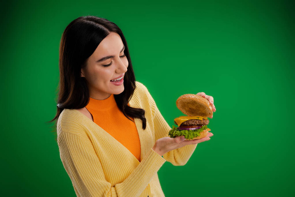 amazed woman looking at tasty burger with cheese and meat isolated on green - Fotó, kép