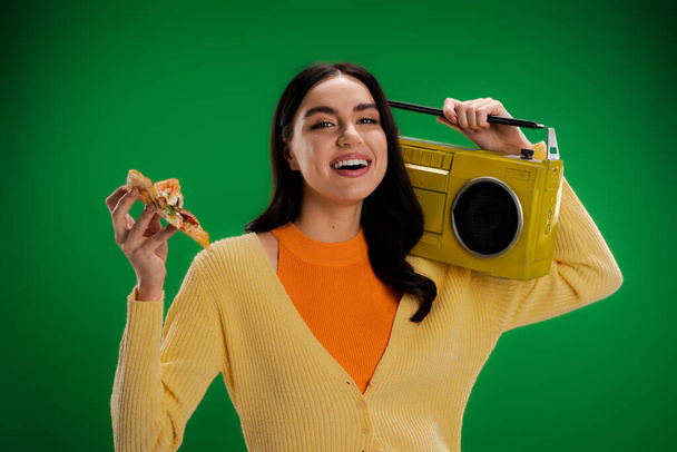 おいしいピザとブームボックスの作品を持つ喜びの女性は緑に隔離されたカメラを見て - 写真・画像
