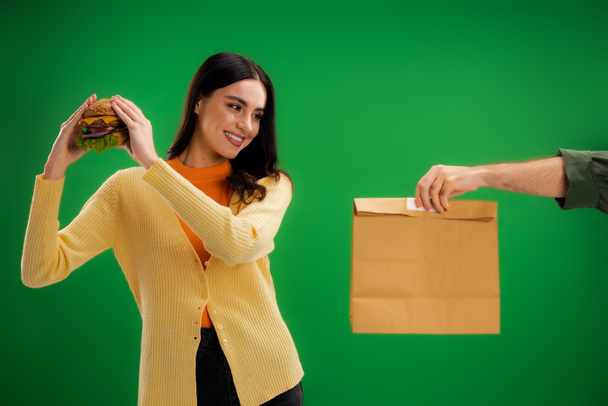 man holding food package near smiling woman with delicious burger isolated on green - Foto, Imagem