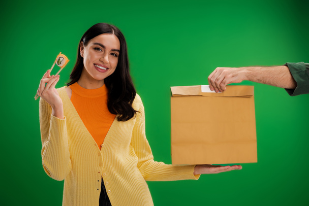 happy woman holding sushi roll with chopsticks near man with paper bag isolated on green - Foto, Imagen