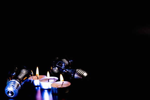 Elektrische Lampe und Kerze auf dunklem Hintergrund. Glühlampe und Kerze. Nein oder Stromausfall. Hohe Strompreise. Strom sparen. - Foto, Bild