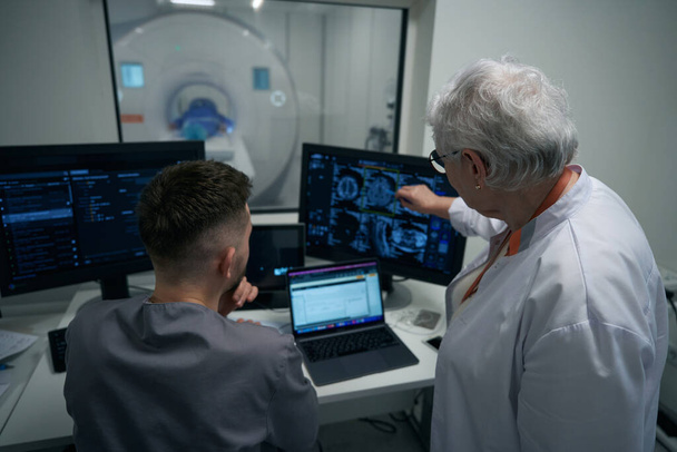 Лікарі, чоловік і жінка, дивляться через МРТ зображення на моніторі комп'ютера, вони досліджують пацієнта. - Фото, зображення