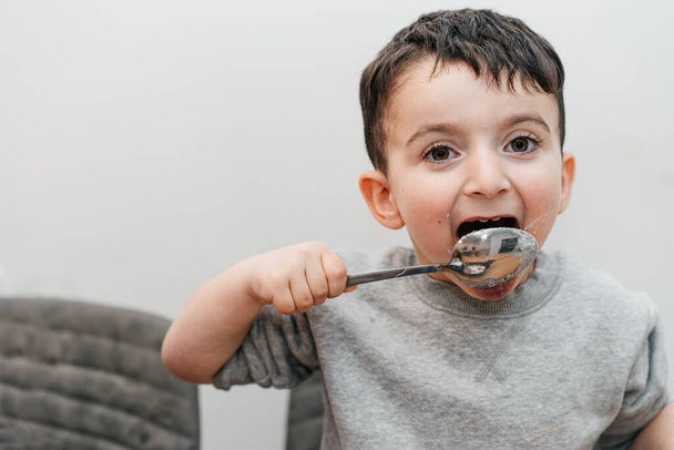 Funny kid licks a spoon with sugar. Portrait joyful beautiful boy eating sugar and looking at camera. - Fotografie, Obrázek