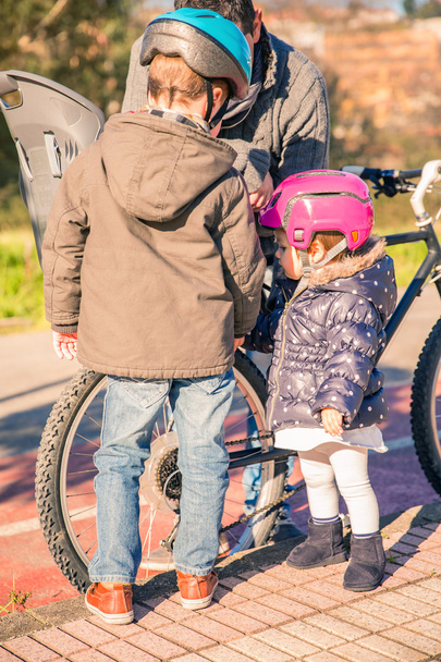 Niños mirando a su padre mientras reparan neumáticos de bicicleta
 - Foto, Imagen