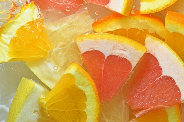 Fresh slices of juicy grapefruit, orange fruit and honey pomelo on white background. Pieces of grapefruit, orange fruit and honey pomelo in sparkling water on white background, closeup. Horizontal image. - Foto, Imagem