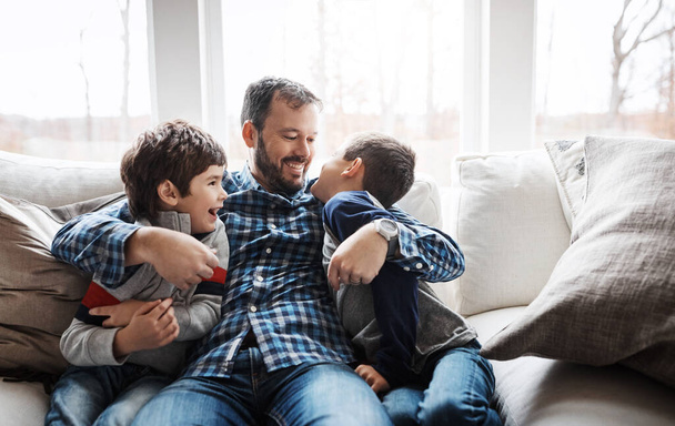 Hug, playful and father with children on the sofa for love, care and relax in their family home. Happy, funny and dad with boy kids for quality time, affection and comedy on the couch of a house. - Photo, Image