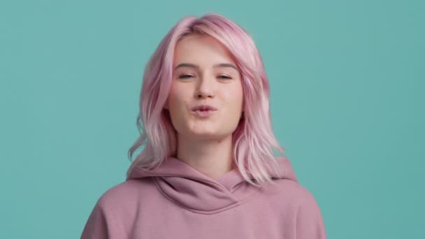 Young fresh creative hipster girl 20s licking plump lips and blowing the air kiss looking straight in camera. Young playful woman face licking sexy lips and flirting. Attractive woman with pink hair - Filmati, video