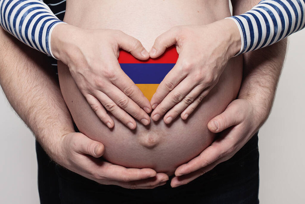 Armenian family concept. Man embracing pregnant woman belly and heart with flag of Armenia colors closeup - Foto, afbeelding