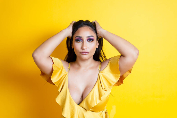 portrait of elegant and sensual hispanic young woman holding her hair in yellow dress - Foto, Bild