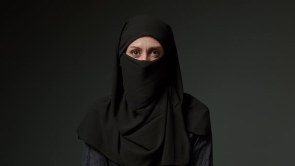 Close-up portrait of a Muslim woman with beautiful eyes in a hijab on a dark background. A girl in a black headscarf is looking at the camera. Arab women showing no. High quality 4k footage - Imágenes, Vídeo