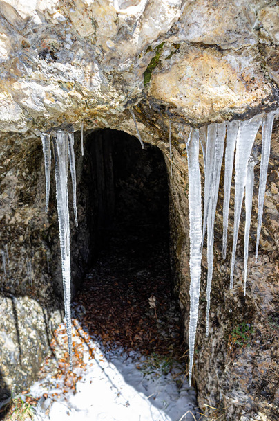 冬の山道の洞窟の入り口に氷の鍾乳石. - 写真・画像