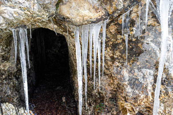 冬の山道の洞窟の入り口に氷の鍾乳石. - 写真・画像