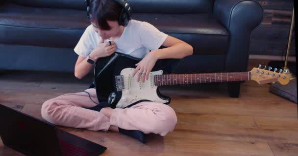 Девочка-подросток с гитарой в наушниках сидит на полу перед ноутбуком. Она слушает звук своей записанной гитары. Медленное движение 4k кадров. - Кадры, видео
