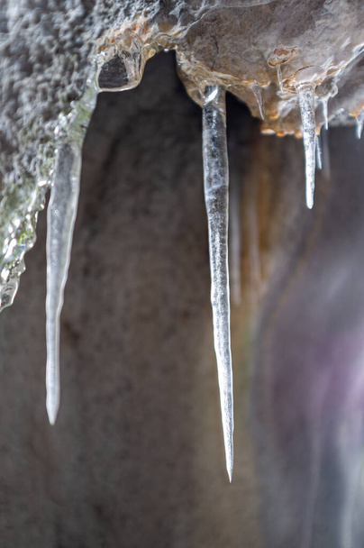 Ice stalactites in the entrance of a cave on a mountain trail in winter. - Foto, Imagen