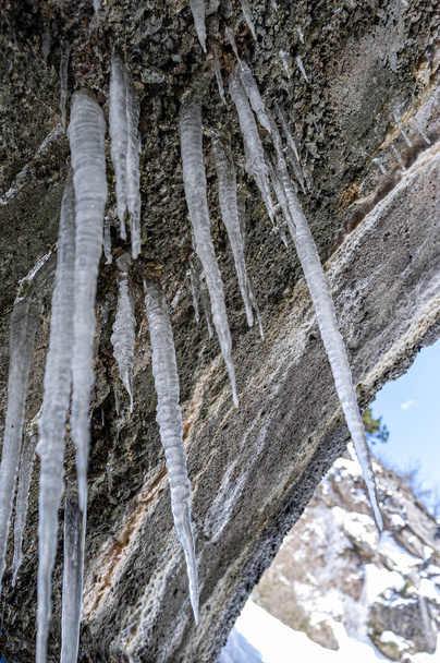 Ice stalactites in the entrance of a cave on a mountain trail in winter. - Fotografie, Obrázek