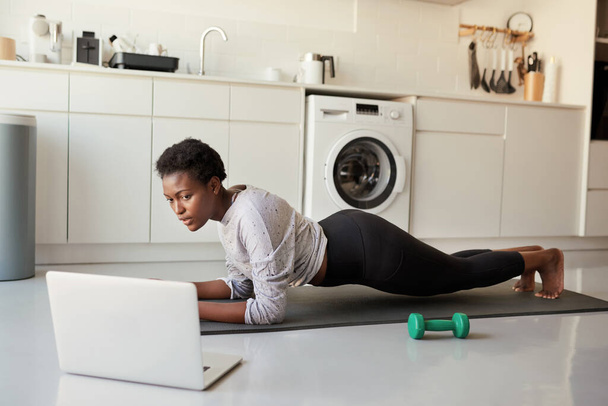 Working out in the comfort of home. a young woman using a laptop while exercising at home - Zdjęcie, obraz
