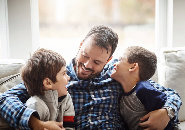 Family home, boys and dad with hug on sofa for conversation, love or bonding for childhood development. Happy people, relax or joke together in living room for fun, happiness or quality time in house. - Photo, image