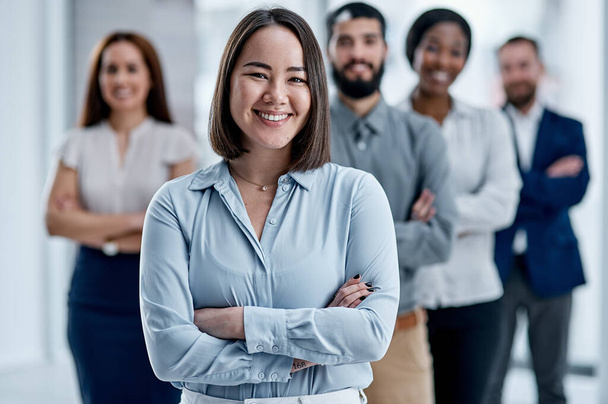 With an enthusiastic team, you can achieve almost anything. Portrait of a businesswoman standing in an office with her colleagues in the background - Zdjęcie, obraz