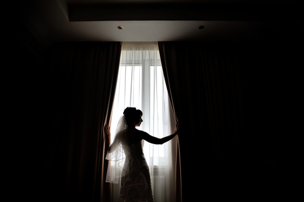silhouette of the bride standing at the window waiting for the w - Foto, afbeelding