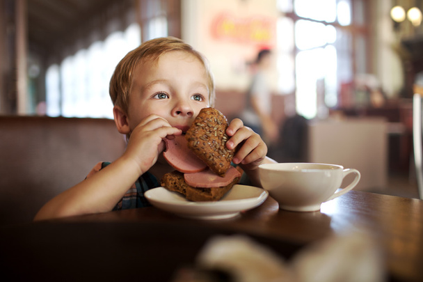 Petit enfant déjeunant avec sandwich et thé au café
 - Photo, image