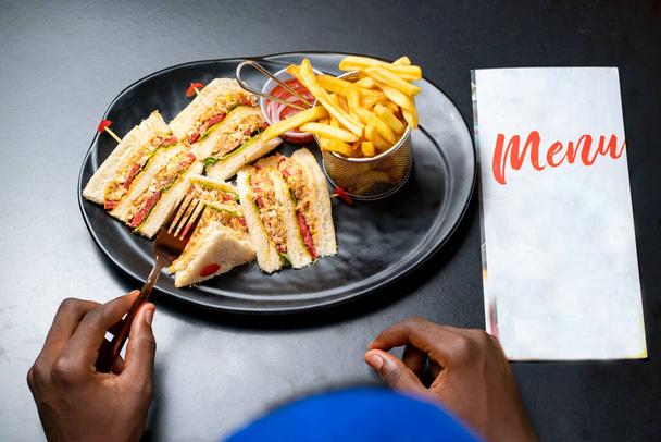 plan view of sliced bread and french fries on a table, with menu notice besides- cropped hand with fork- served meal on a table - Foto, imagen