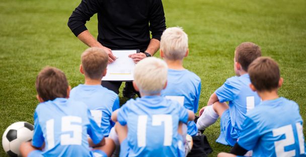 子供のサッカーのサッカー試合。男の子と緑の草の上に座ってコーチ. - 写真・画像