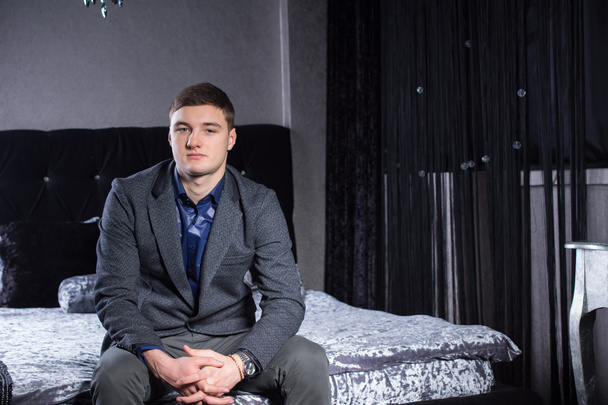 Νεαρός άνδρας στην επίσημη ένδυση κάθεται στο κρεβάτι - Φωτογραφία, εικόνα