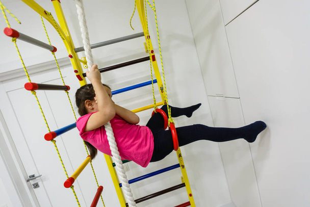 Children Activity Concepts. Little Caucasian Girl Having Stretching Exercises on Wall Bars Indoors - Photo, Image