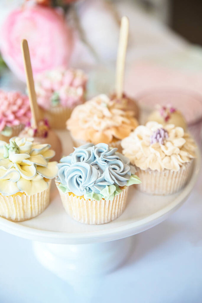 パーティーテーブル、結婚式、ベビーシャワー、ハイティー、誕生日の休日の背景にプレート上で提供ホイップクリームと装飾的な花のアイシングを持つ新鮮なカップケーキ - 写真・画像
