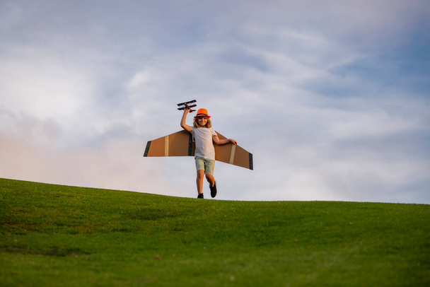Little child boy is playing and dreaming of flying over the clouds. Pilot aviator child with a toy airplane plays on summer nature. Child playing with plane wings. Concept of dreams and travels - Φωτογραφία, εικόνα