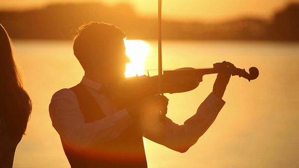 Skrzypce duet mężczyzna i kobieta gram na skrzypcach na charakter na zachód słońca nad jeziorem - Materiał filmowy, wideo