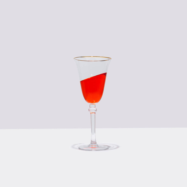 A glass of red cocktail stands straight with the drink  in it is tilted at an angle. Surreal drinking culture, summer party or celebration composition. - Photo, image