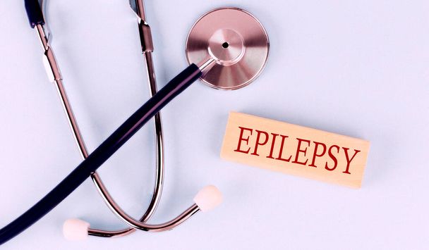On a blue background, stethoscope and wooden block with the word EPILEPSY .Medical concept - Valokuva, kuva