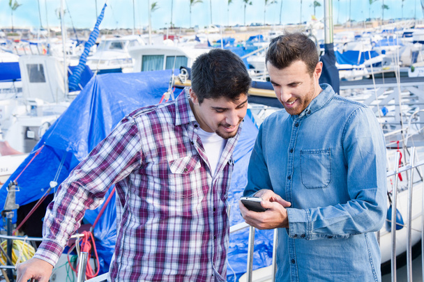Двоє друзів дивляться на мобільний телефон на пристані
 - Фото, зображення
